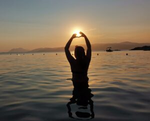 Images of girl in the sunset doing a heart sign with her hands